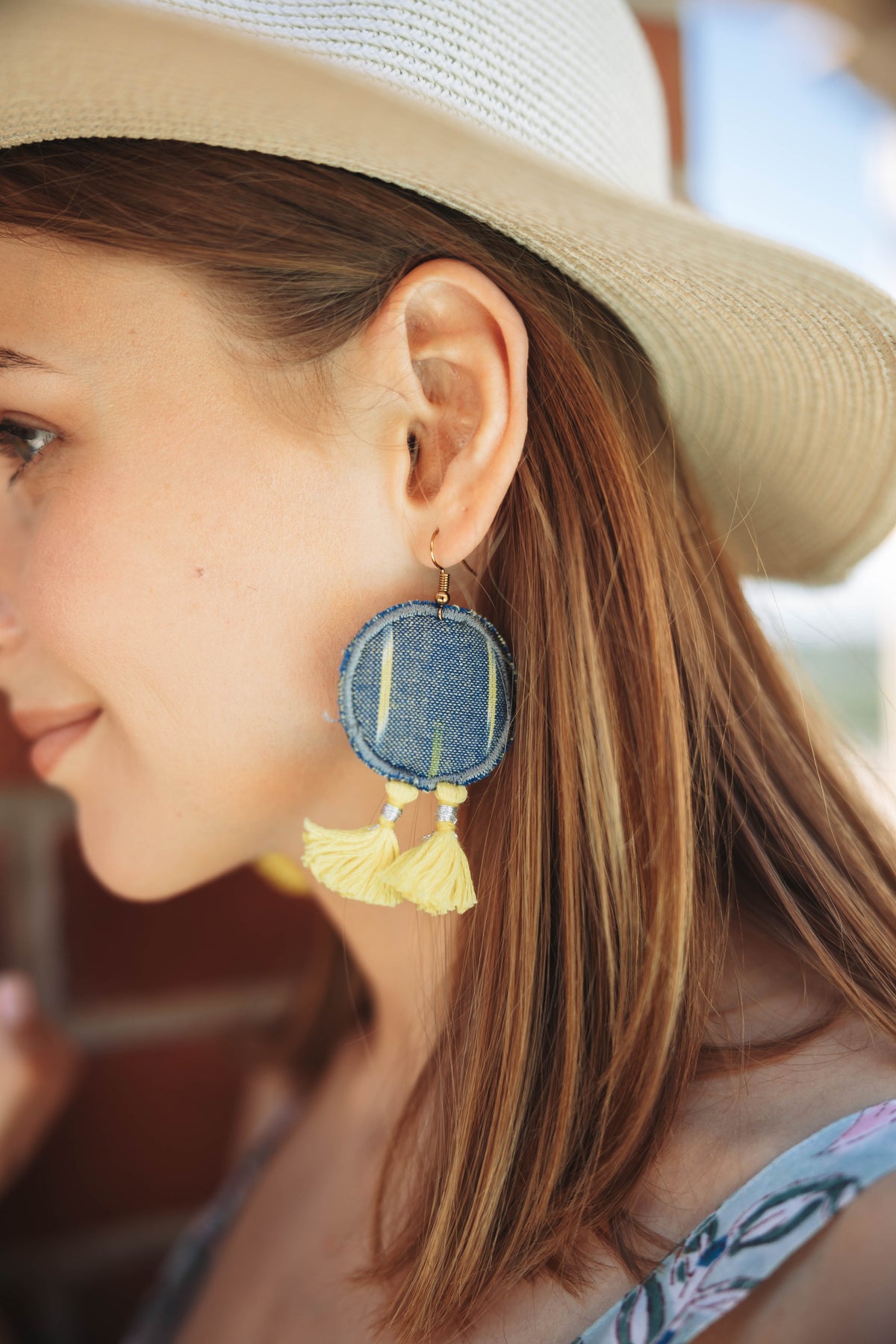 Woman wearing round tassel drop earrings in IKAT pattern iin gray and yellow